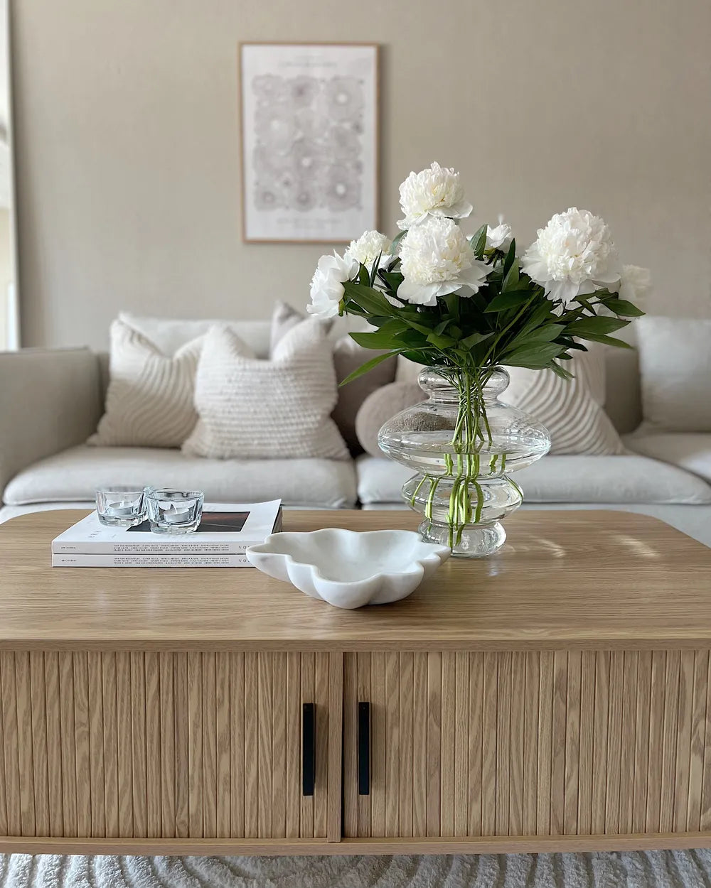 Living room with a wooden coffee table, white flowers in a vase, and a gray sofa.
