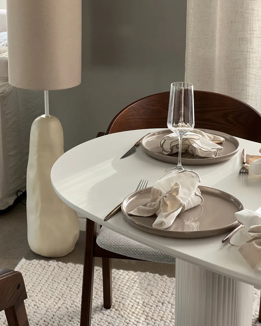Dining table set with plates, glasses, and cutlery in a room with a lamp and curtains.