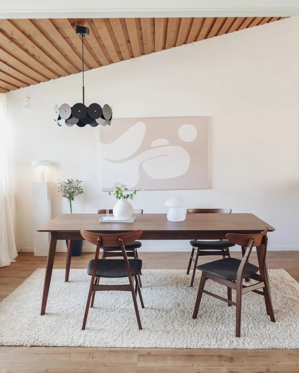 Dining room with wooden table and chairs on a white rug, abstract painting on the wall.