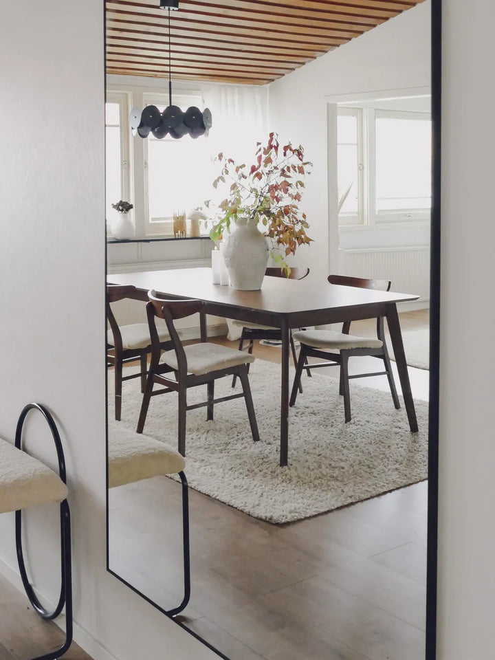 Dining room with a wooden table and chairs, large mirror on the wall, and decorative elements.