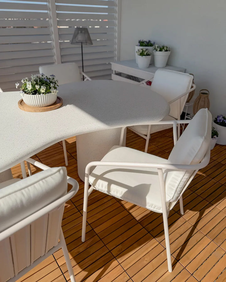 Outdoor dining area with white furniture and potted plants on a wooden deck.