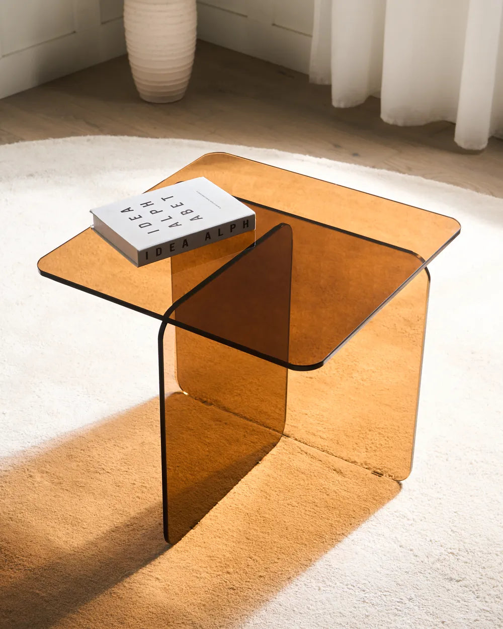 Clear glass side table with a book on a white rug
