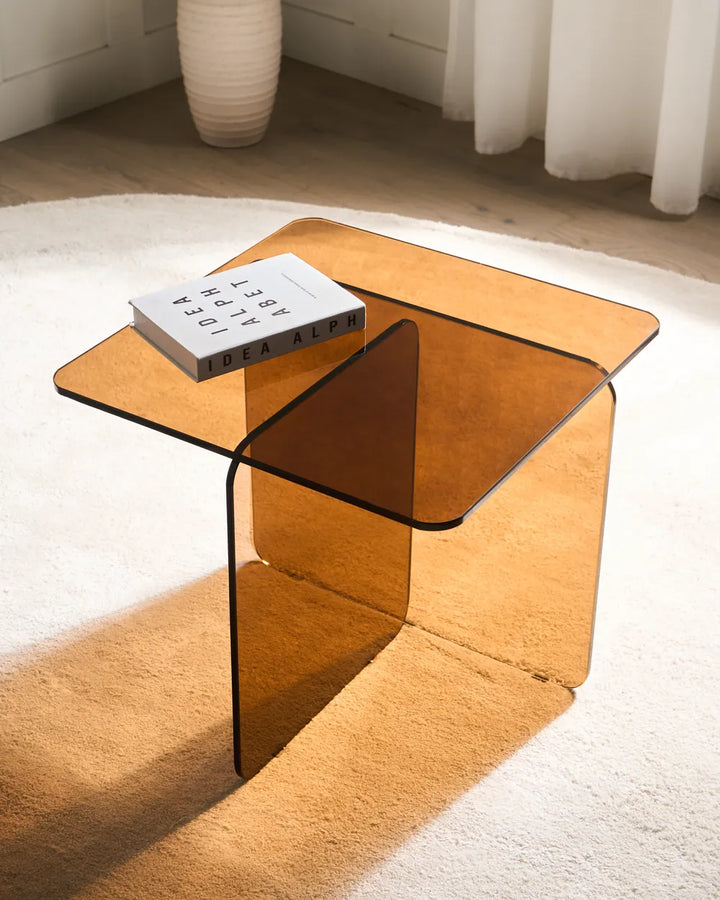 Clear glass side table with a book on a white rug