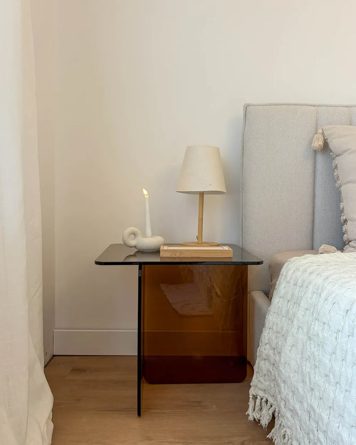 Bedroom with a nightstand featuring a lamp and candle next to a bed with white bedding.