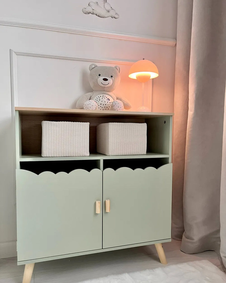 Children's cabinet with storage baskets and a teddy bear in a softly lit room.