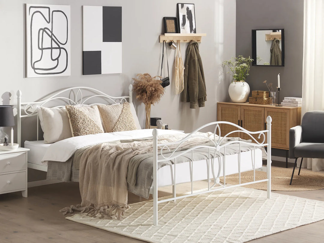 Modern bedroom with a white metal bed, decorative pillows, and a wooden side table.