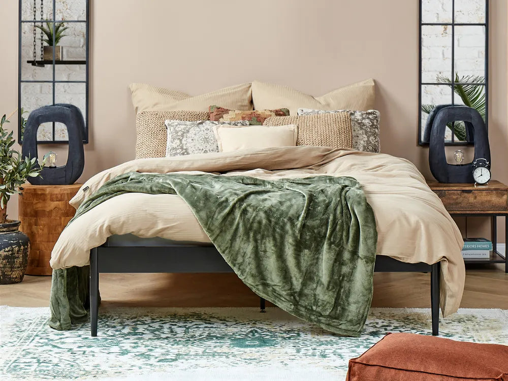 Bedroom with a bed featuring a green blanket and beige bedding, surrounded by decorative items.