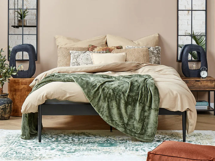 Bedroom with a bed featuring a green blanket and beige bedding, surrounded by decorative items.