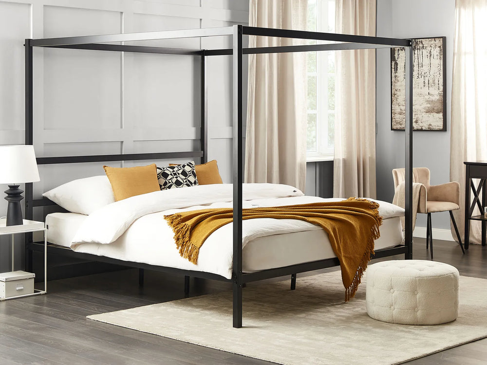 Black metal canopy bed in a bedroom setting with white bedding and a yellow blanket.