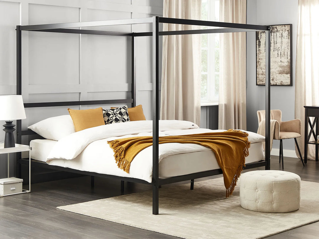 Black metal canopy bed in a bedroom setting with white bedding and a yellow blanket.