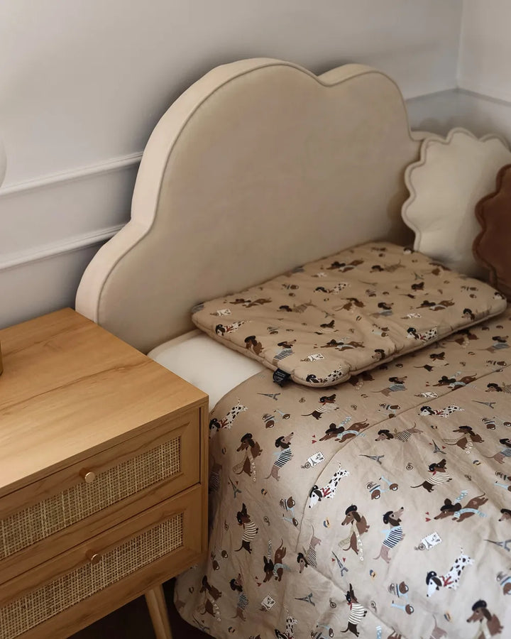 Beige bedspread with cartoon characters on a bed next to a wooden nightstand.