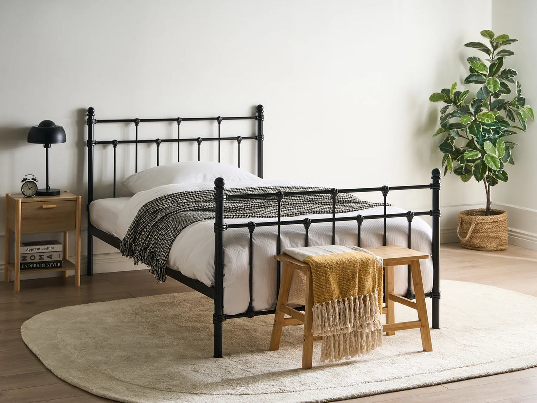 Bedroom with a black metal bed, wooden nightstand, and plant.