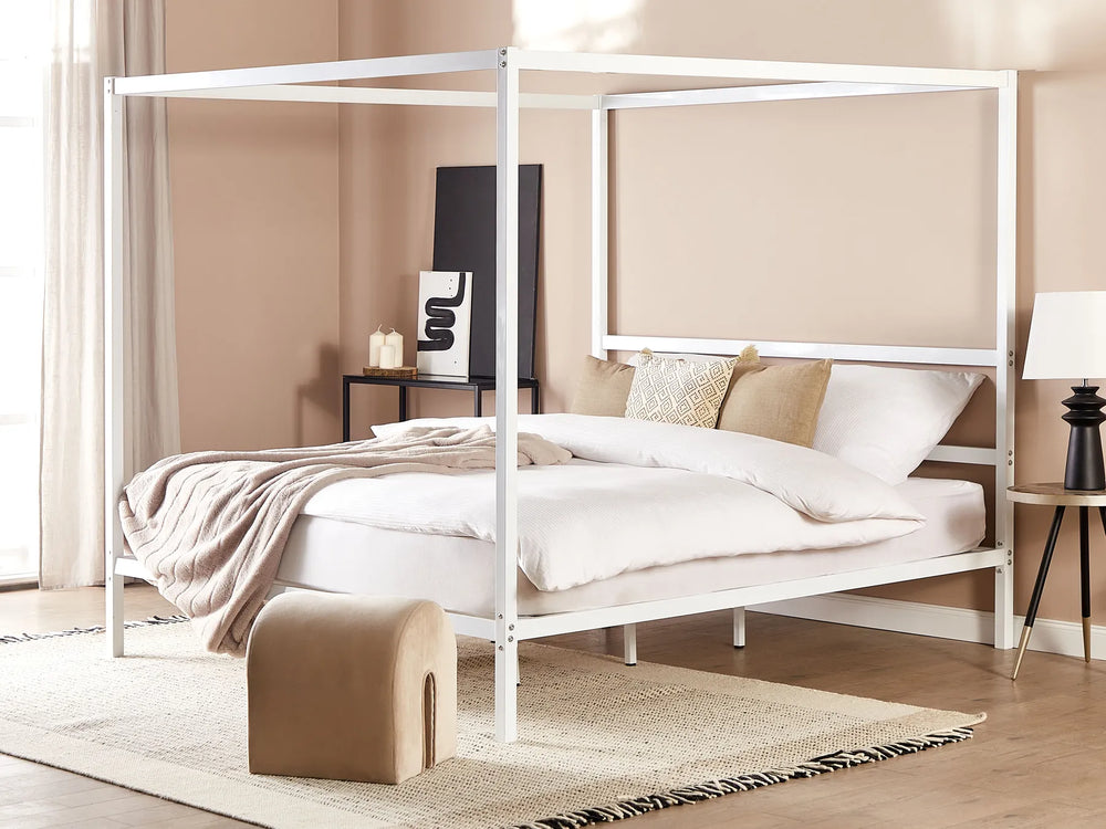 White metal canopy bed in a room with beige walls and wooden flooring.