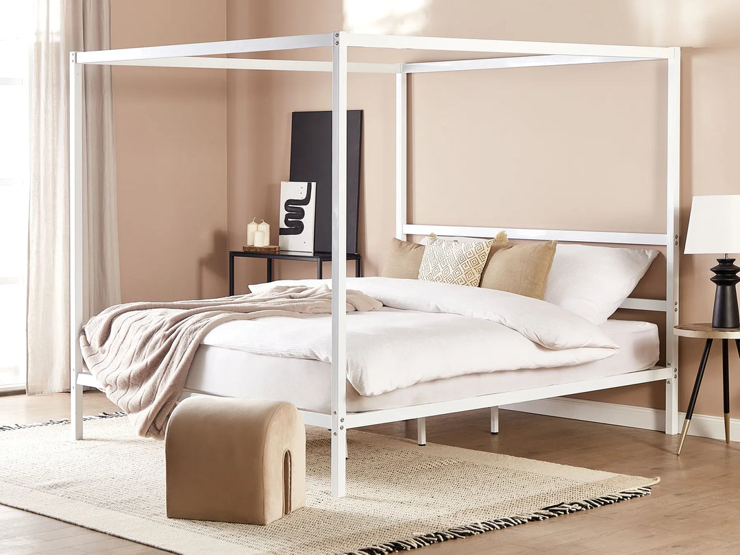White metal canopy bed in a room with beige walls and wooden flooring.