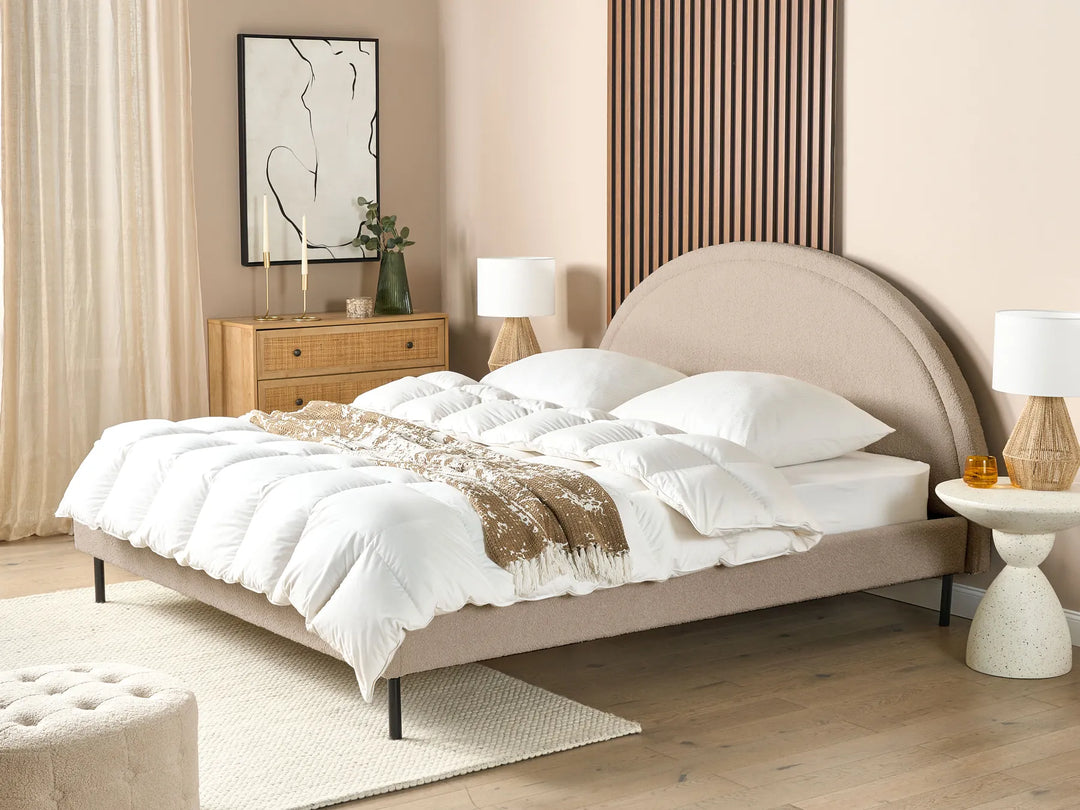 Neatly made bed in a bedroom with beige walls and wooden furniture.