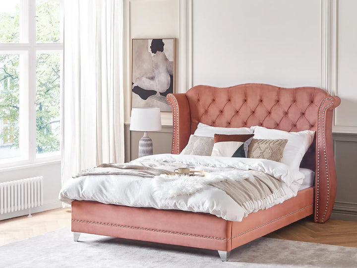 Pink upholstered bed in a bedroom with a window and artwork on the wall.