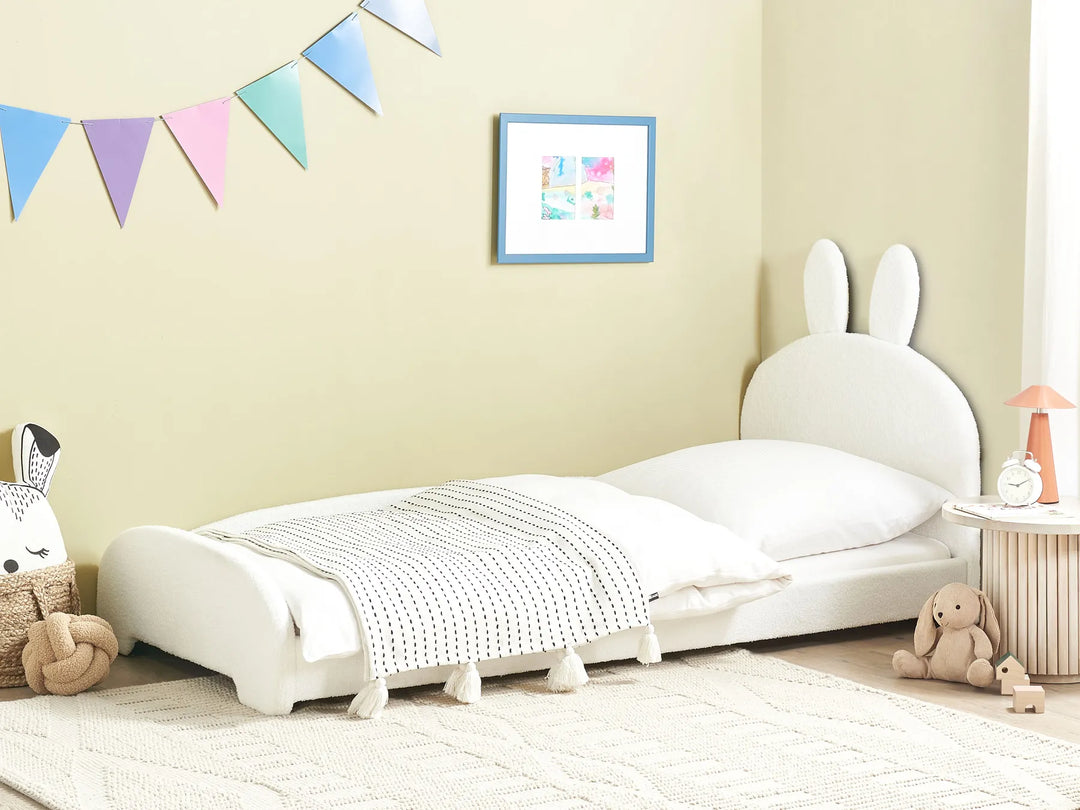 Children's room with a white bed featuring bunny ears, colorful flags, and toys.
