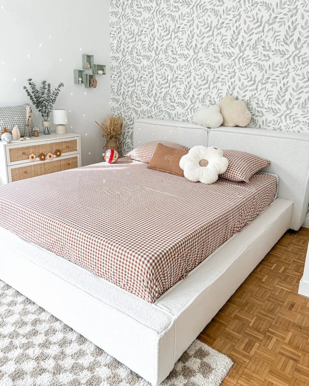 Neatly made bed with checkered brown and white bedding in a bedroom with patterned wallpaper.