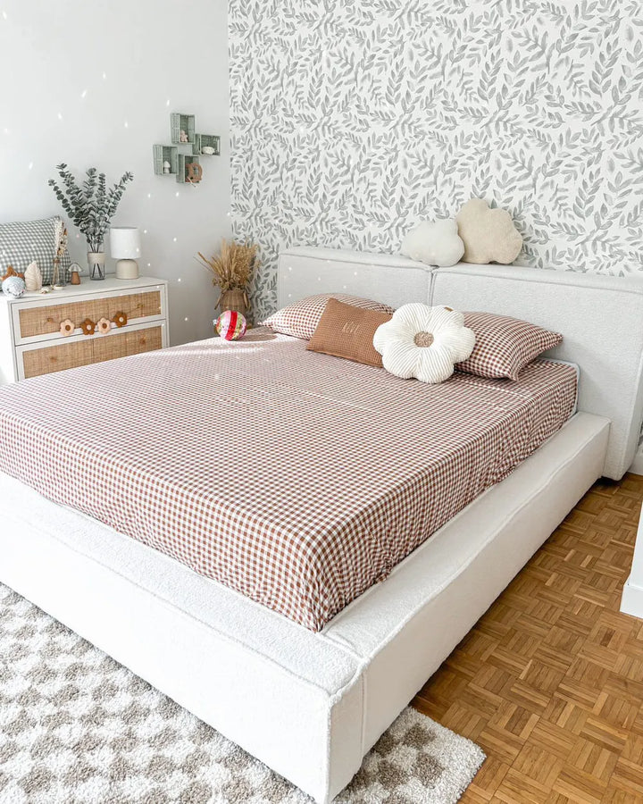 Neatly made bed with checkered brown and white bedding in a bedroom with patterned wallpaper.