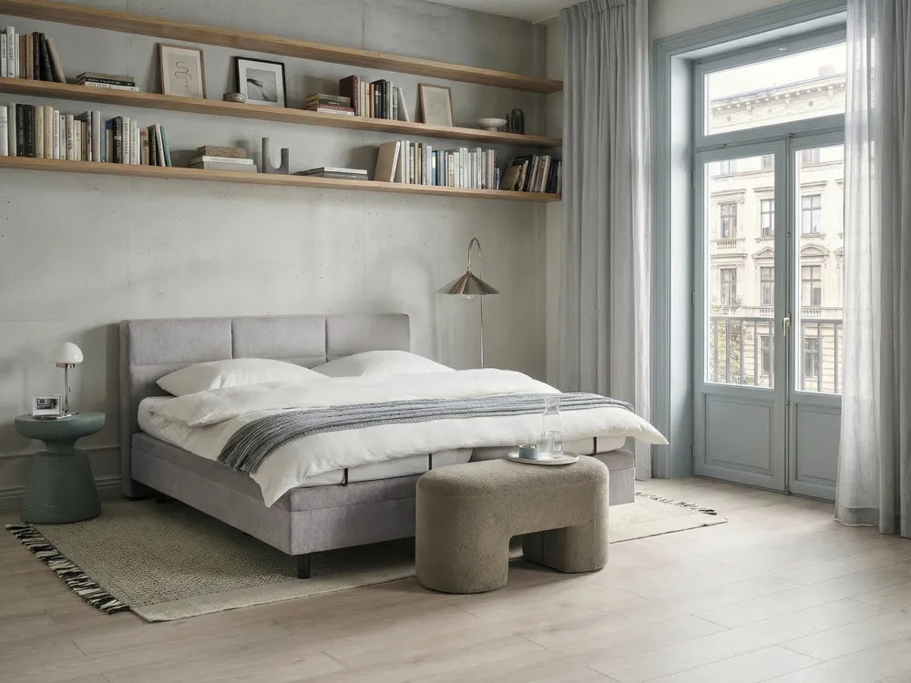 Modern bedroom with gray upholstered bed, wooden shelves, and large window.