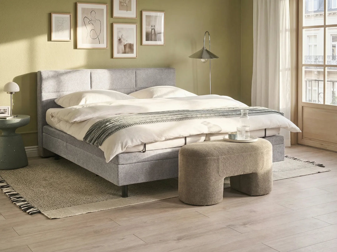 Modern bedroom with a gray upholstered bed, side table, and ottoman.