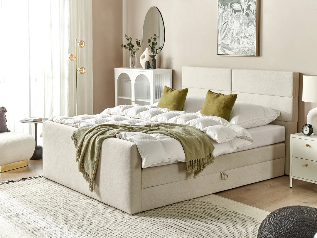Beige upholstered bed with white bedding and green throw in a bedroom setting.