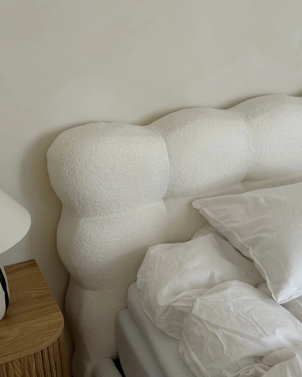 White textured headboard with pillows and a wooden nightstand in a bedroom setting.