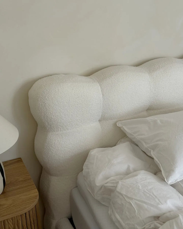 White textured headboard with pillows and a wooden nightstand in a bedroom setting.