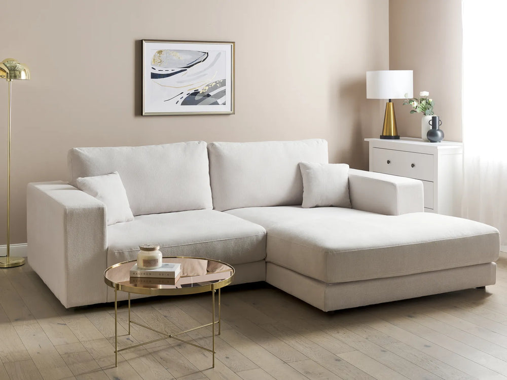 Beige sectional sofa in a living room with a side table and lamp.
