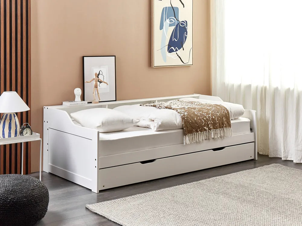 White bed with drawers in a room with beige walls, a lamp, and artwork.