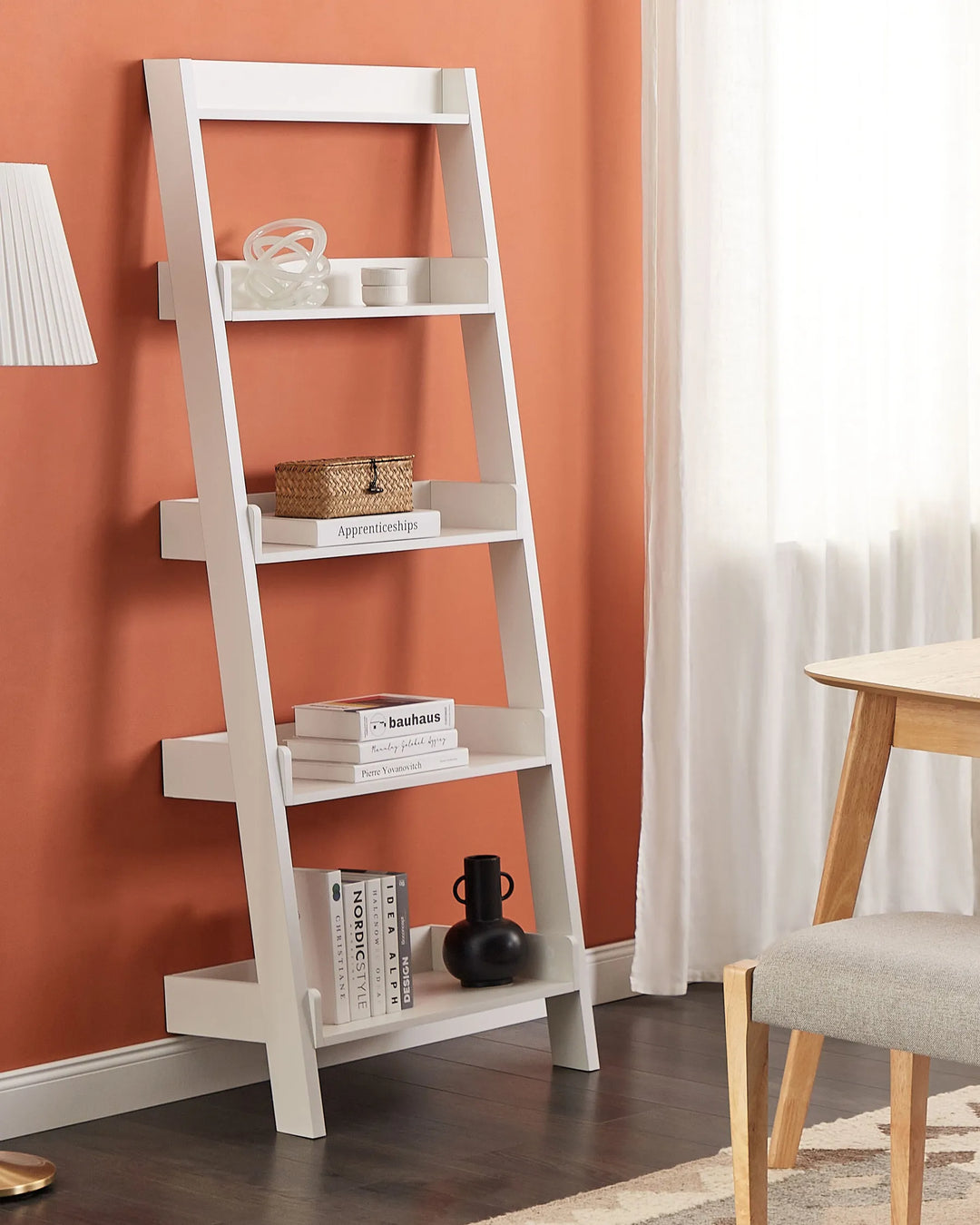 White ladder shelf against an orange wall with books and decor items.