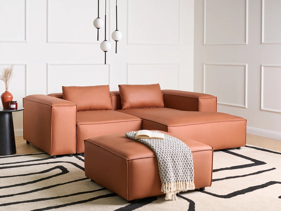 Brown leather sectional sofa in a living room with a white wall and decorative rug.