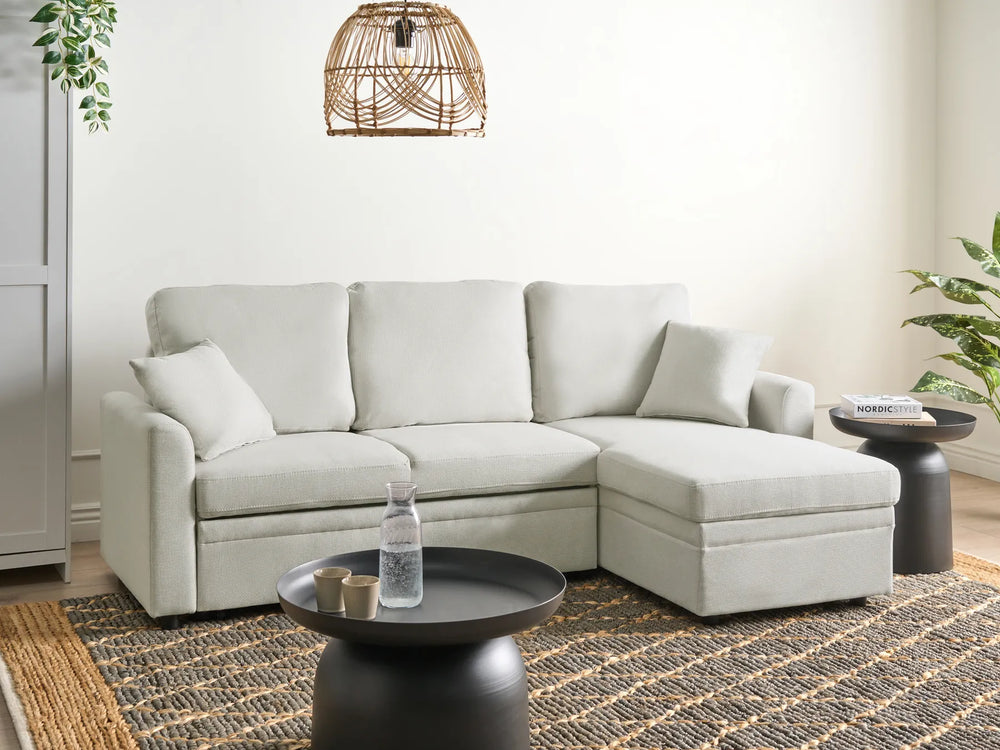 Light gray sectional sofa in a living room setting with a rug and small tables.