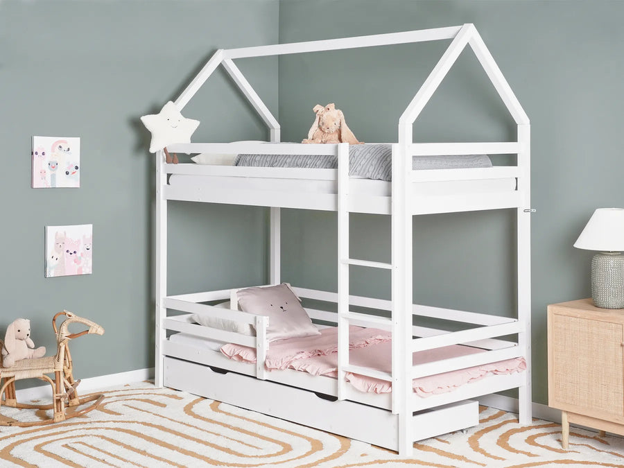 White children's house-shaped bed with pink bedding in a room with a gray wall and wooden floor.