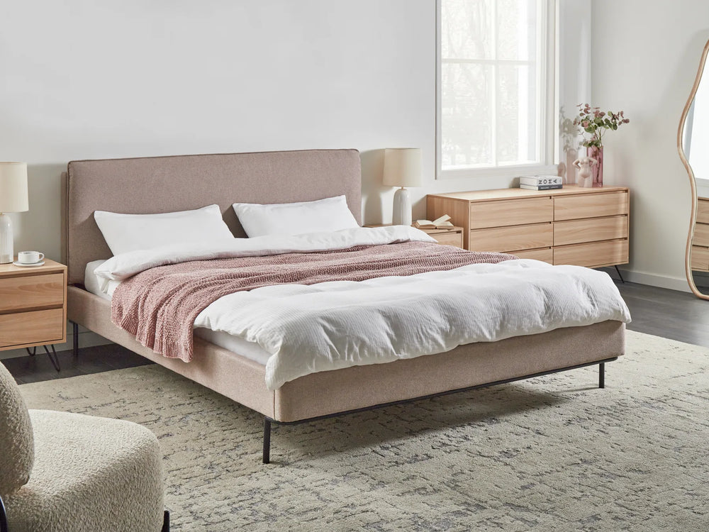 Beige upholstered bed with white bedding and pink blanket in a bedroom setting.