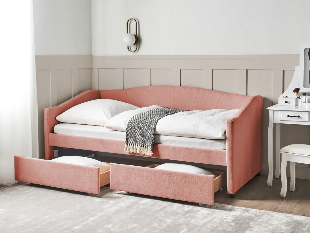 Pink upholstered bed with storage drawers in a room setting.