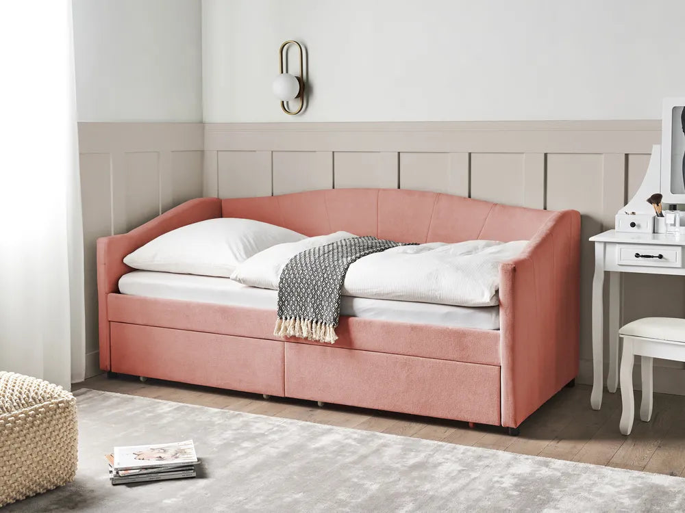 Pink upholstered bed in a bedroom setting with a white nightstand and chair.
