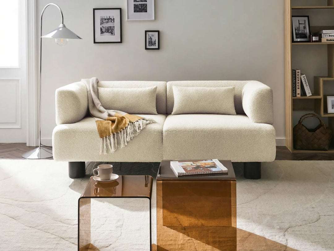 Beige sofa in a living room with a coffee table and books on a shelf.