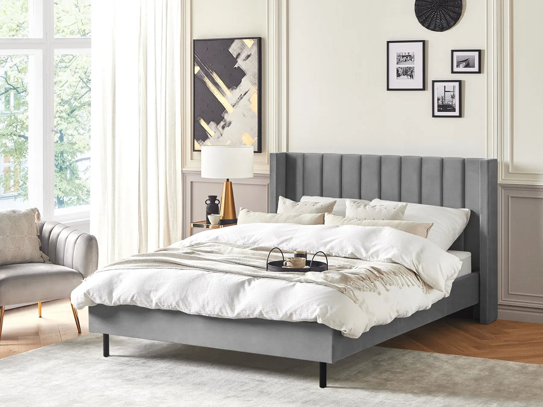 Gray upholstered bed in a bedroom with a lamp and decor.