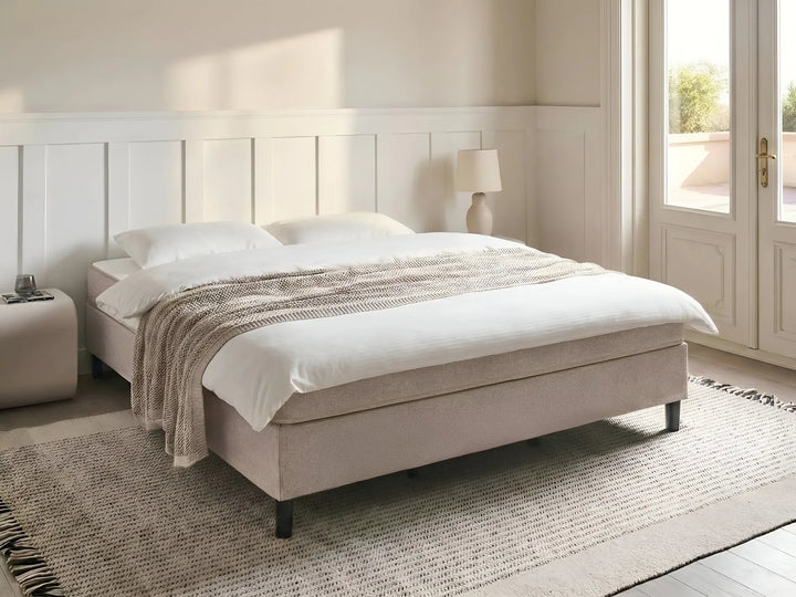 Beige bed with white bedding in a bright bedroom