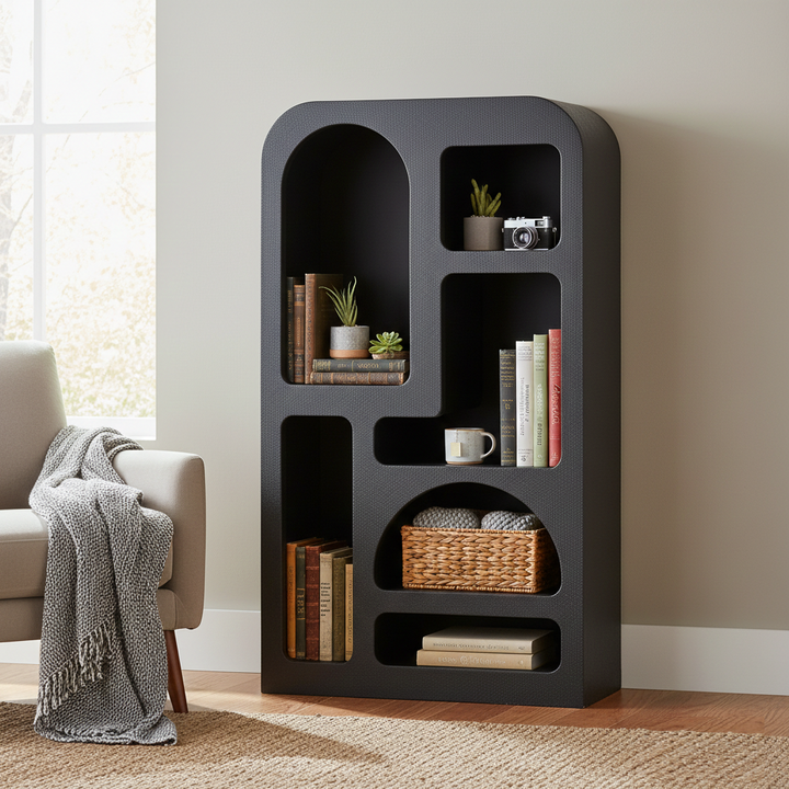 Black bookshelf with decorative items in a room with a gray sofa and window.
