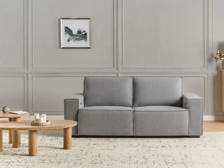 Gray sofa in a living room with wooden coffee tables and a framed picture on the wall.