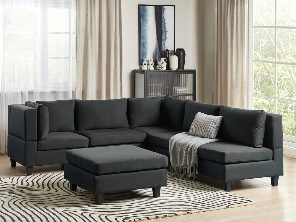 Black sectional sofa in a living room with a striped rug and a side table.