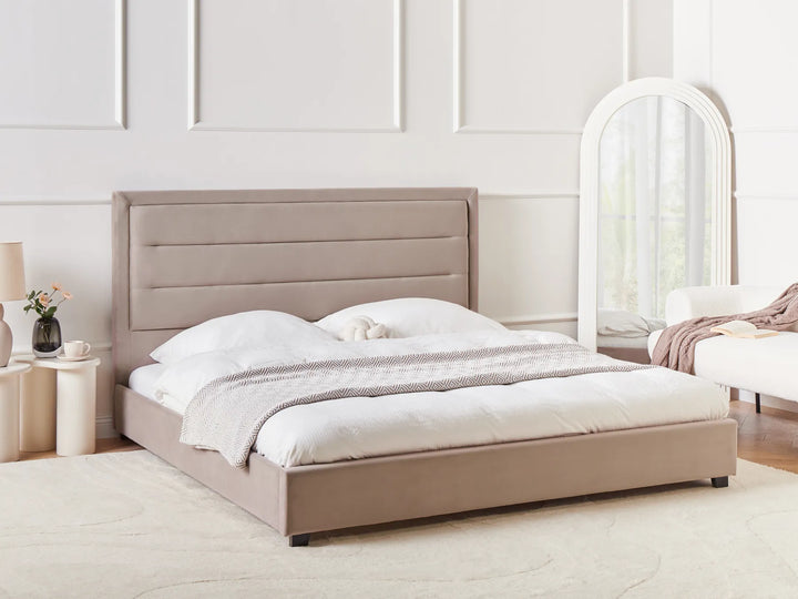 Beige upholstered bed in a minimalistic bedroom with a mirror and side table.