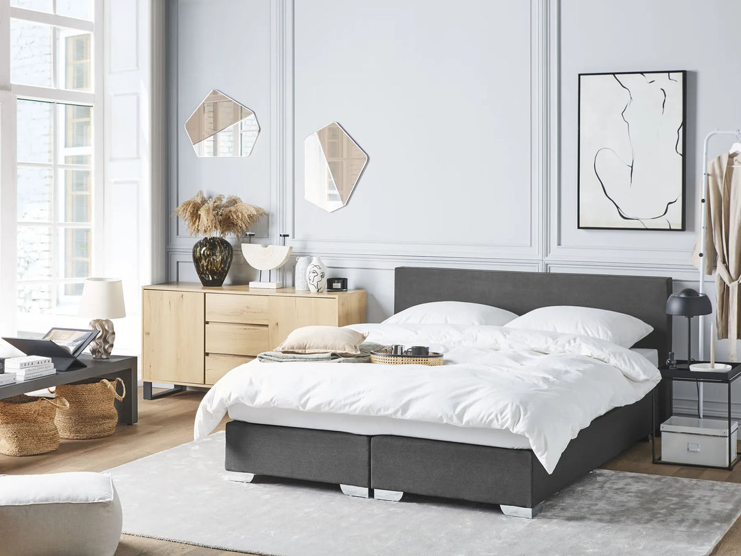 Modern bedroom with a gray bed, wooden sideboard, and decorative elements.