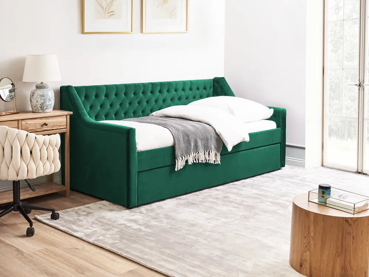 Green upholstered bed in a room with a desk and lamp.