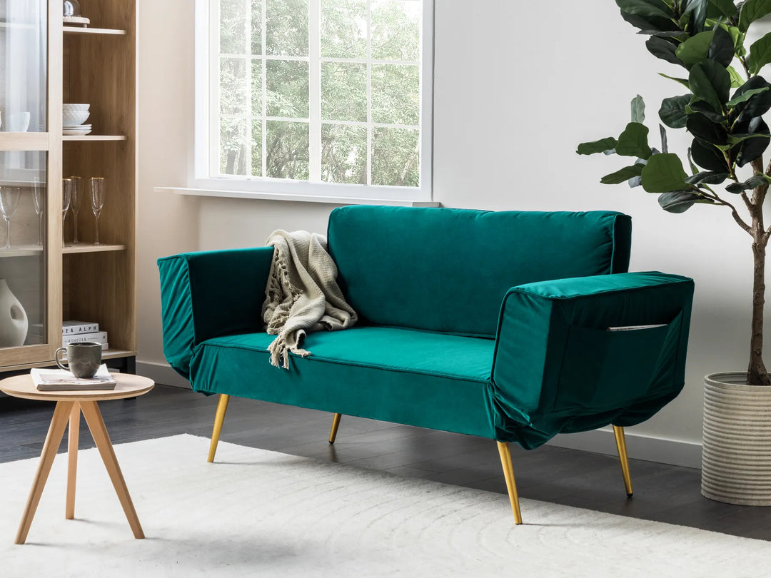 Teal sofa in a living room with a plant and small table.