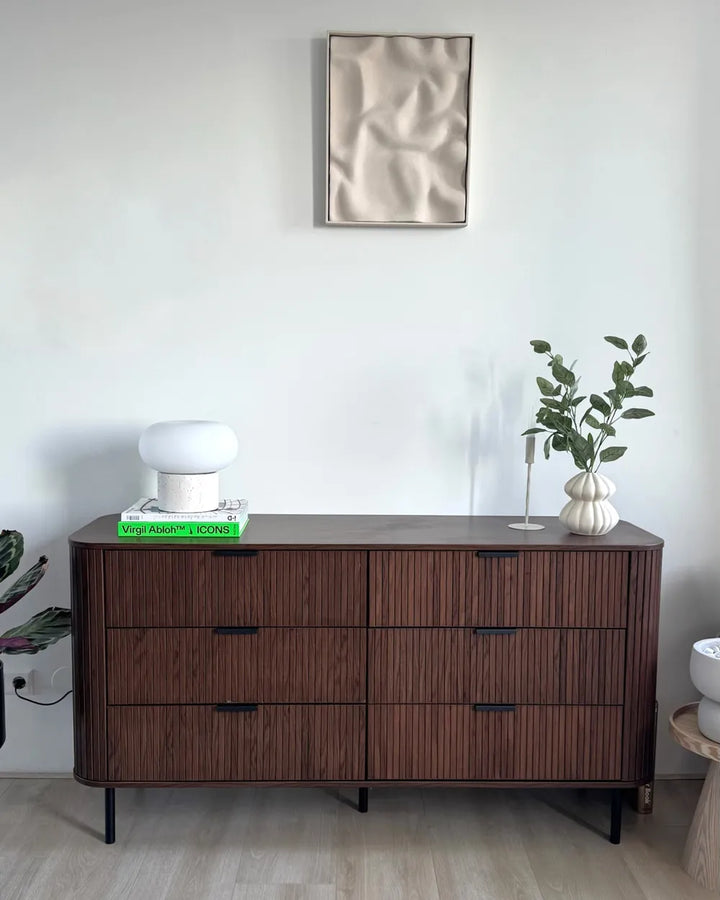 Wooden dresser with decorative items in a room with a mirror on the wall.