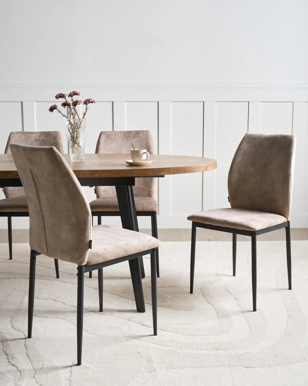 Taupe fabric dining chairs with tall backrests and black metal legs arranged around a dining table in a bright, modern dining space with minimalist décor.