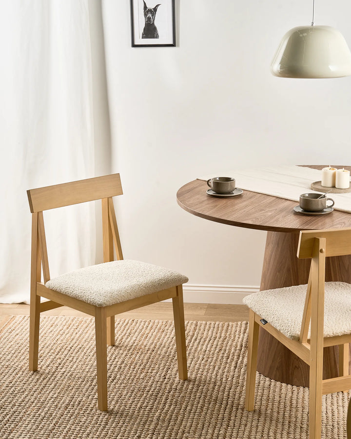 Light wood dining chairs with cream bouclé seats styled around a round wooden dining table in a warm, minimalist dining space with neutral tones, soft lighting, and cozy textured décor.